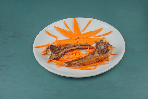 Grilled lamb chops on white plate with carrot slices.