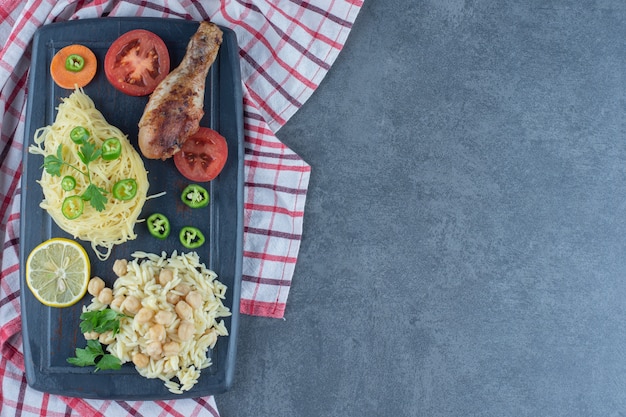 Grilled leg, spaghetti and rice on dark board. 