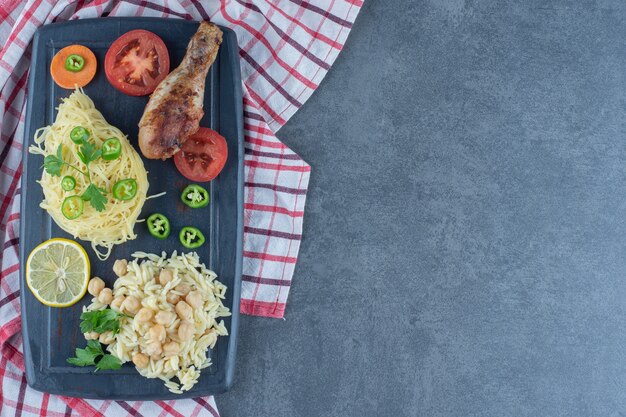 Grilled leg, spaghetti and rice on dark board. 