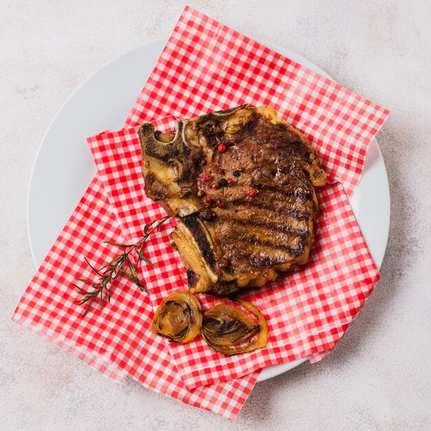 Grilled meat on plate with checkered towel