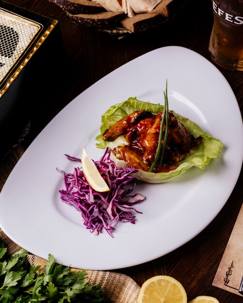 Grilled meat in teriyaki sauce in lettuce leaf with red cabbage salad and lemon.