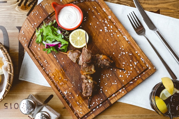 Grilled meat on wooden sticks salt sour cream lemon radish lettuce top view