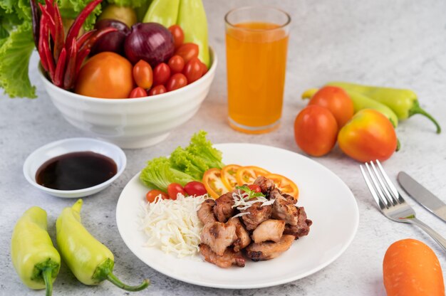 Grilled pork cutlet with tomatoes and salad, arranged in a white dish.