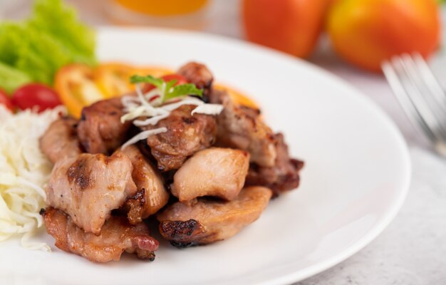 Grilled pork cutlet with tomatoes and salad, arranged in a white dish.