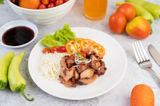 Grilled pork cutlet with tomatoes and salad, arranged in a white dish.