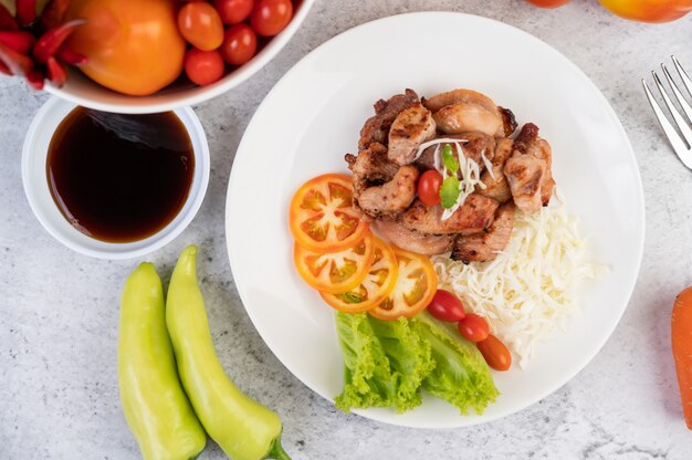 Grilled pork cutlet with tomatoes and salad, arranged in a white dish.