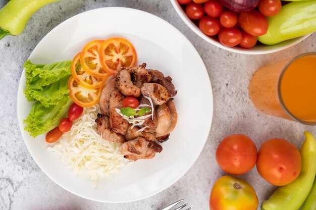 Grilled pork cutlet with tomatoes and salad, arranged in a white dish.