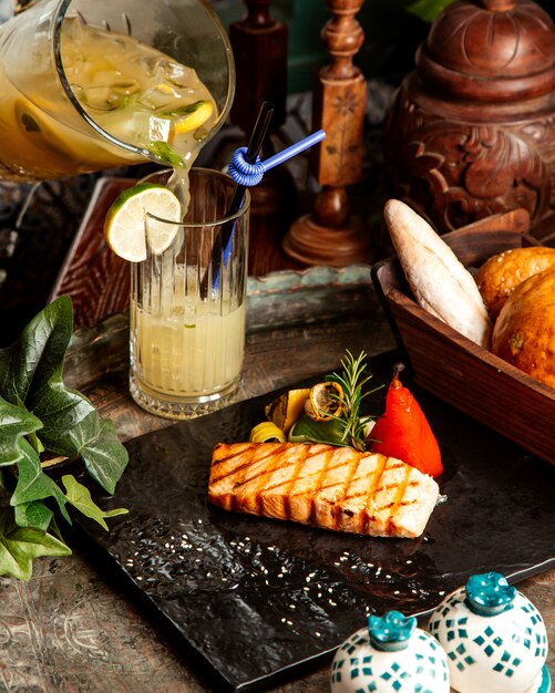 Grilled salmon steak with grilled vegetables lemon rosemary homemade lemonade and bread on table