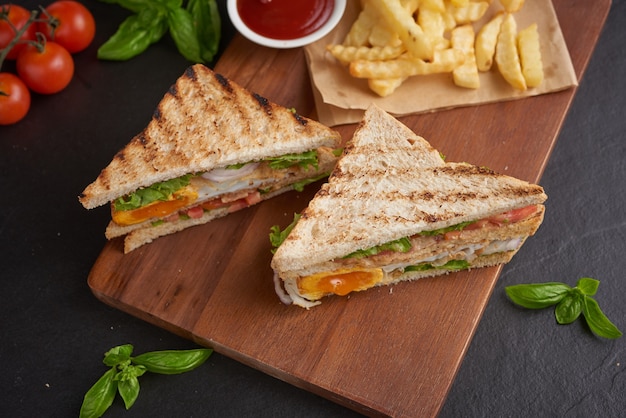 Grilled and sandwich with bacon, fried egg, tomato and lettuce served on wooden cutting board