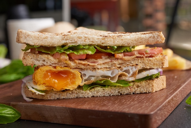 Grilled and sandwich with bacon, fried egg, tomato and lettuce served on wooden cutting board