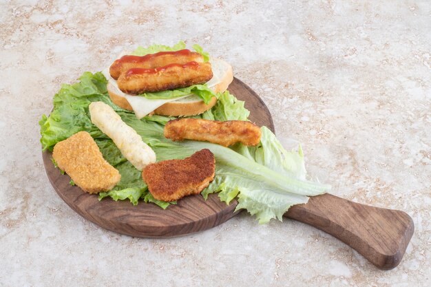 Колбаски на гриле, сырные палочки и куриные нагреты на листе салата.