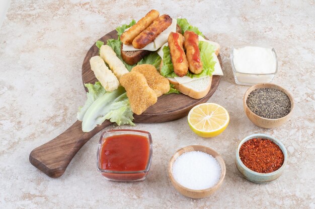 Grilled sausages with chicken nuggets on a piece of lettuce on a wooden board with sauces aside.