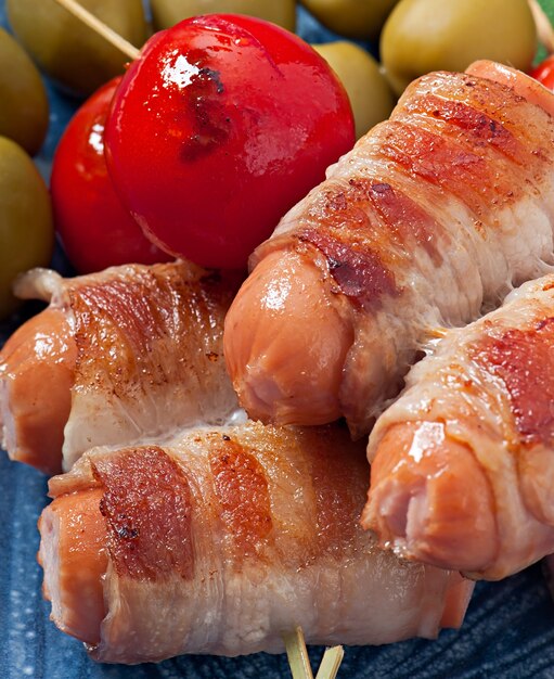 Free photo grilled sausages wrapped in strips of bacon with tomatoes and sage leaves