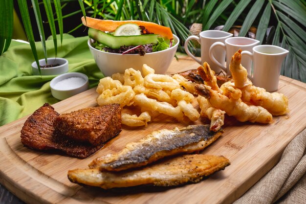 Grilled seafood on wooden board fish prawns calamary green salad side view