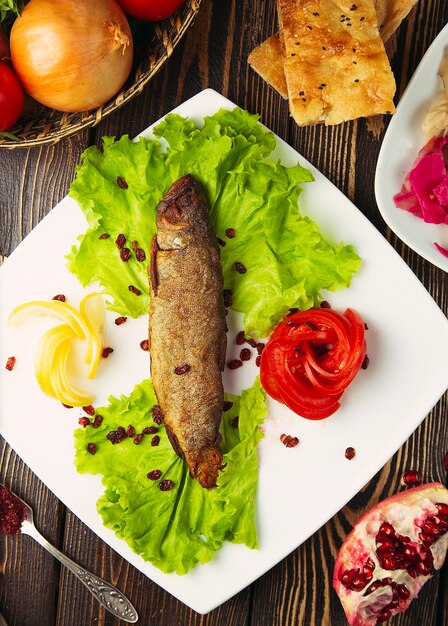 Grilled silver fish served with lemon, lettuce, tomato and pomegranate seeds. 