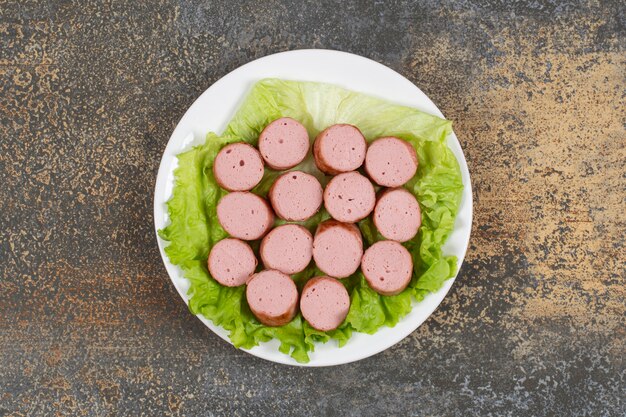 Grilled sliced sausages and lettuce on white plate.