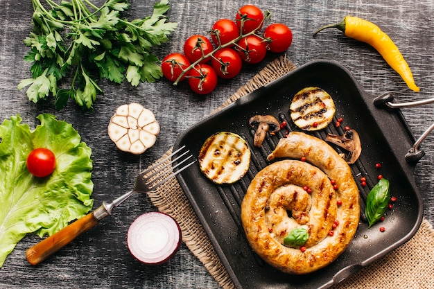 Grilled snail sausages in pan with spices and vegetable on wooden grey backdrop