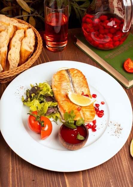 하얀 접시에 그린 샐러드, 토마토, 레몬, 레드 딥 소스와 구운 흰 연어 생선 필렛