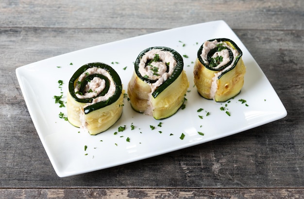 Grilled zucchini rolls stuffed with cream cheese and tuna on wooden table