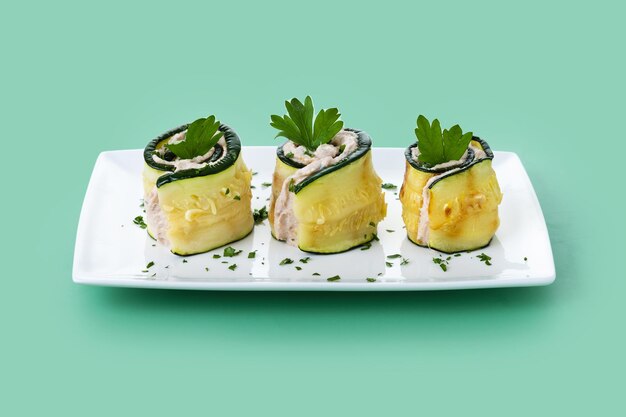 Grilled zucchini rolls with tuna and cream cheese on green background