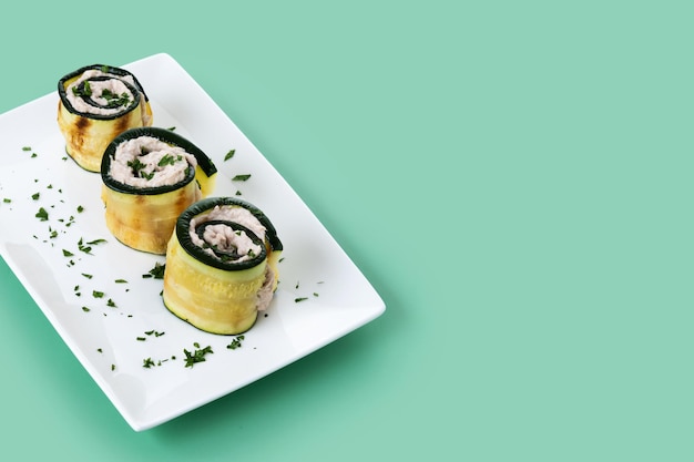 Grilled zucchini rolls with tuna and cream cheese on green background