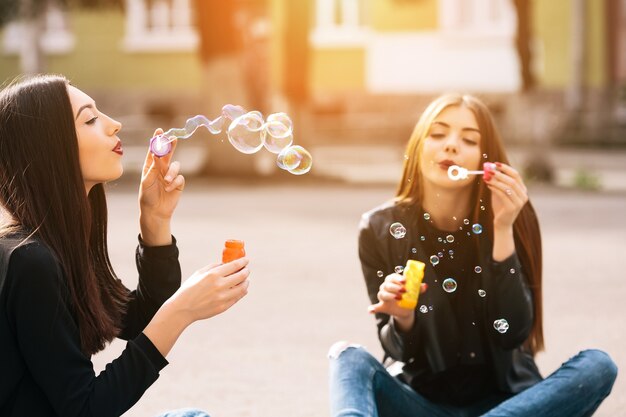 Grils sitting on the floor blowing bubbles