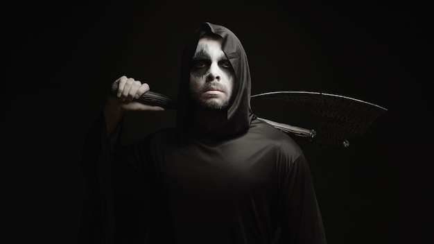 Grim reaper over black background with axe in his hands. Halloween costume.