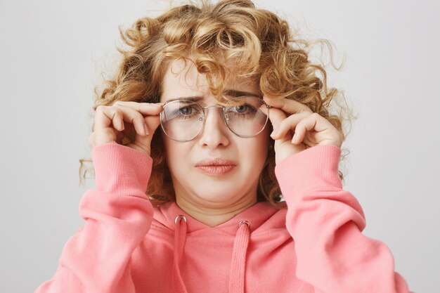 Grimacing confused girl put on glasses, frowning puzzled