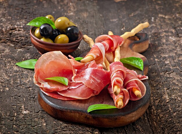 Grissini bread sticks with ham, olives, basil on old wooden