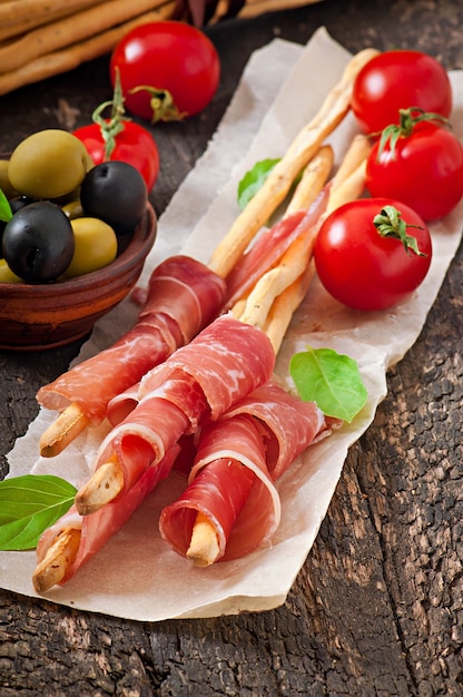 Grissini bread sticks with ham, olives, basil on old wooden