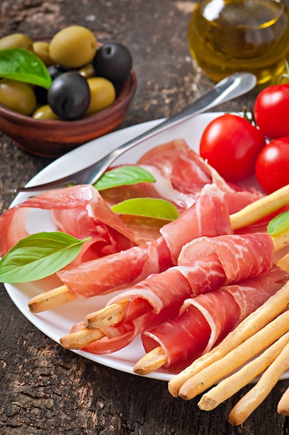 Grissini bread sticks with ham, olives, basil on old wooden