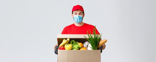Groceries and packages delivery covid19 quarantine and shopping concept friendly courier in face mask and gloves delivering food box to client house during coronavirus contactless deliver