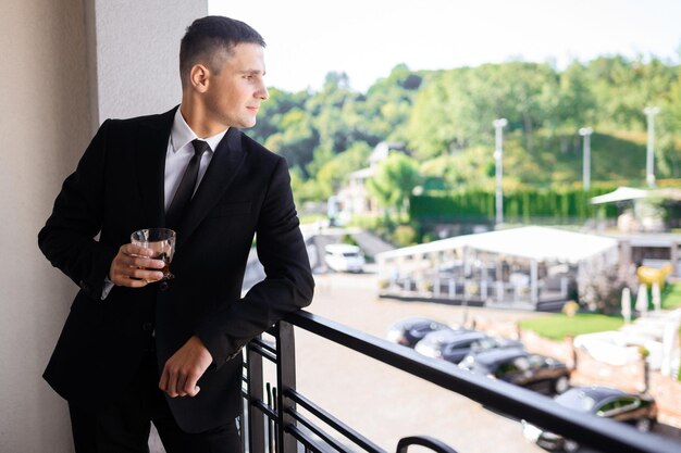 Groom on balcony holding glass engjoying sunny weather on balcony