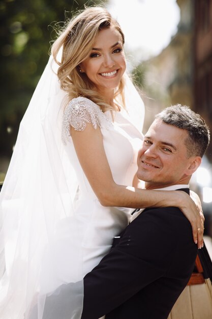 Groom in black tuxedo hugs tender stunning bride while they stan