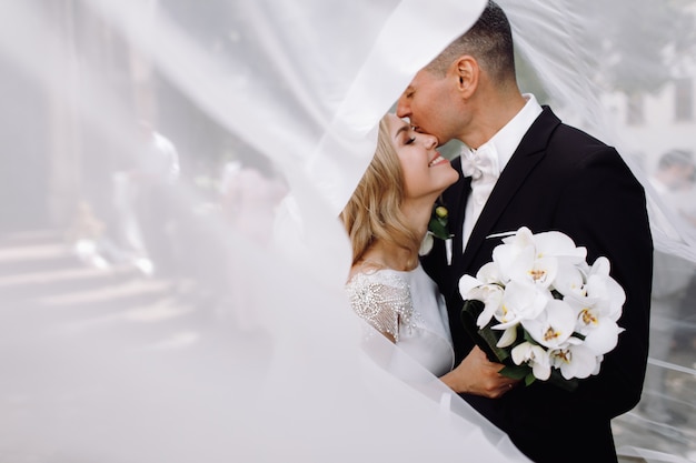 Free photo groom in black tuxedo hugs tender stunning bride while they stand