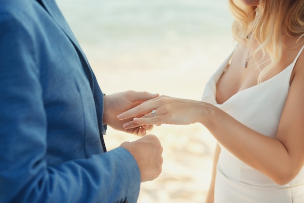 Жених в синем костюме ставит обручальное кольцо на руке невесты