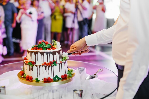 Жених и невеста держат нож, пока они режут свадебный торт