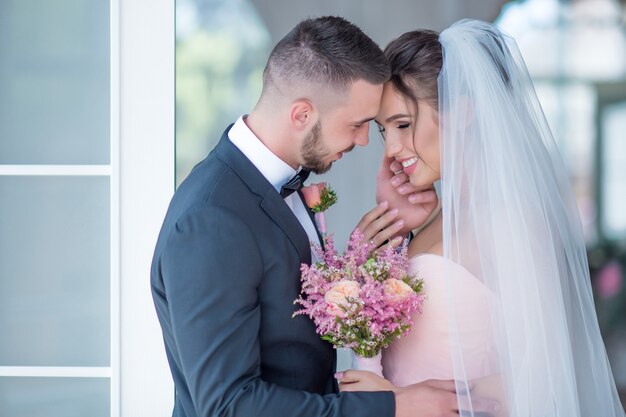 Groom and bride in a pink dress hold each other with love standing in a room