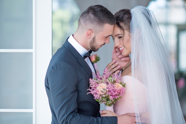 Groom and bride in a pink dress hold each other with love standing in a room