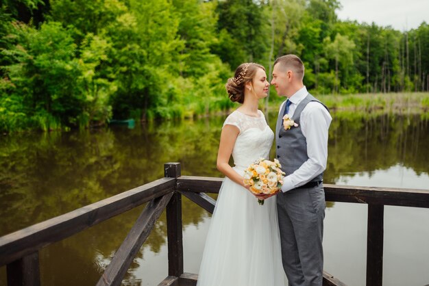 신랑과 신부 웨딩 드레스는 호수에 나무 베란다를 얻는다.