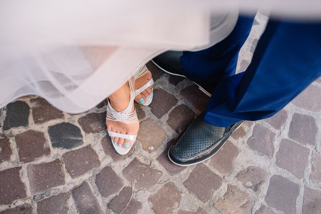 Groom and bride in white shoes stand on the street