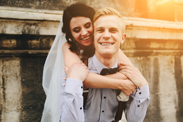 Groom carries bride on his back, outdoors