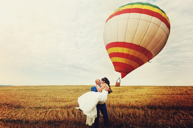 Groom holds bride in his arms while wind blows away air balloon