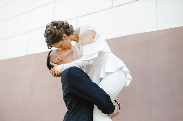 Жених держит невесту на руках и целует ее