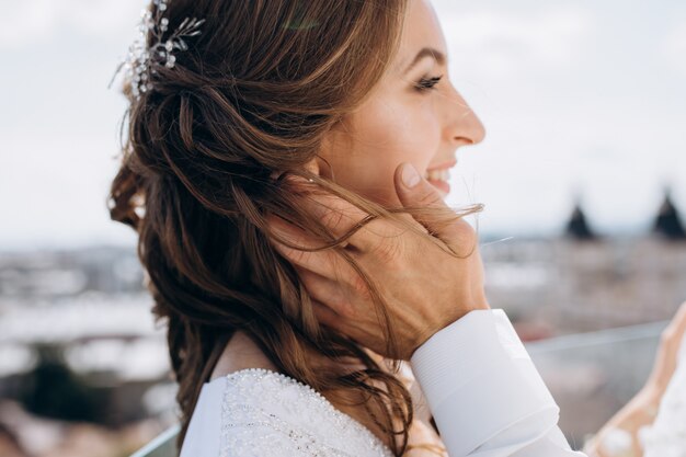 Groom holds bride tender standing on the roof with great summer cityscape around them