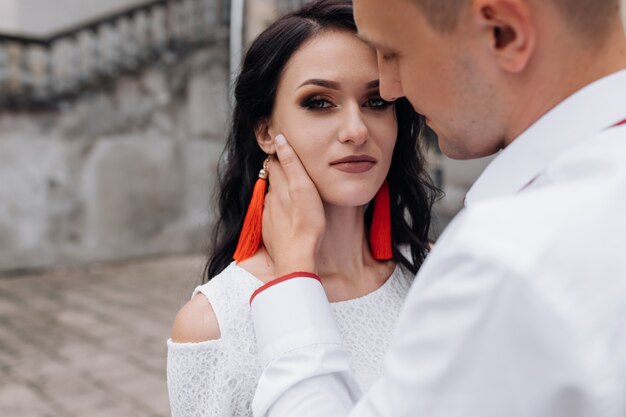 Groom holds tender face of a brunette bride with red lips