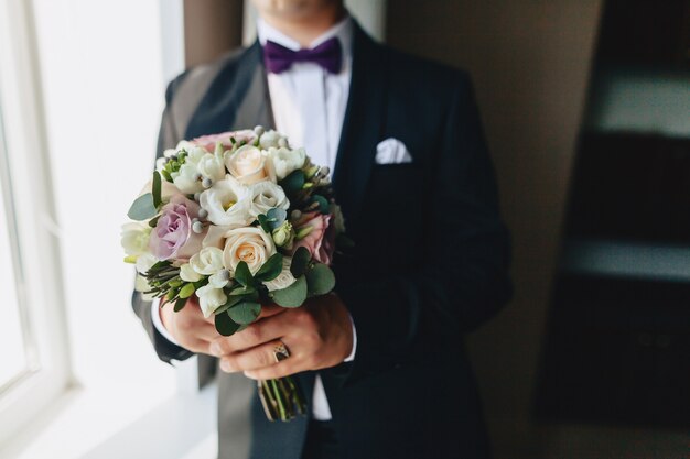 The groom holds a wedding bouquet in his hands