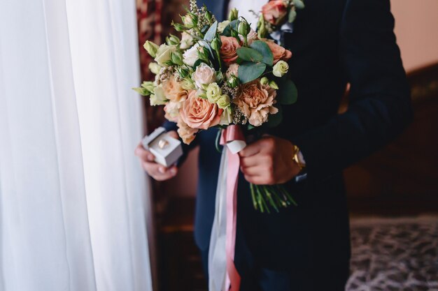 The groom holds a wedding bouquet in his hands