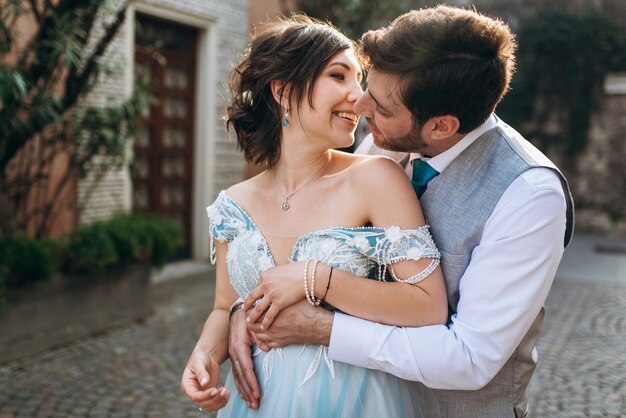 Groom hugs bride tender from behind kissing on the street