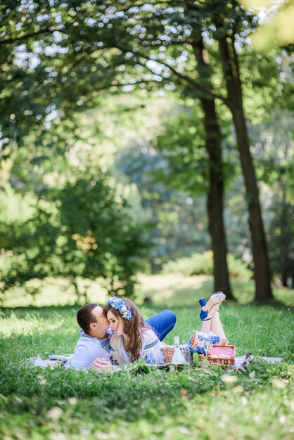 Groom hugs bride tender lying with her on the blanket during picnic in a green park